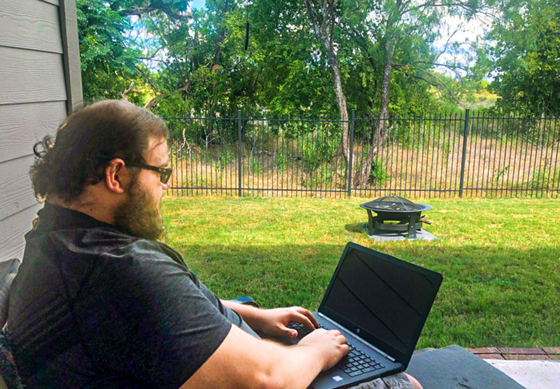 male student sitting on porch typing on laptop